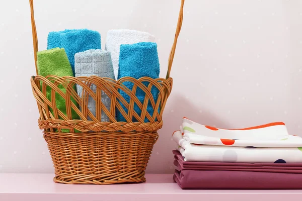 On the dresser there is a stack of clean ironed bed linen and there is a basket in rolls of folded multicolored towels