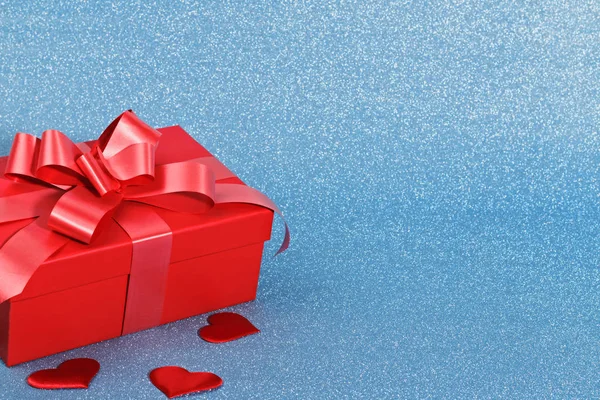 Closeup de uma caixa vermelha com um presente e corações em um fundo azul brilhante com espaço de cópia. Conceito de celebração do dia dos namorados — Fotografia de Stock