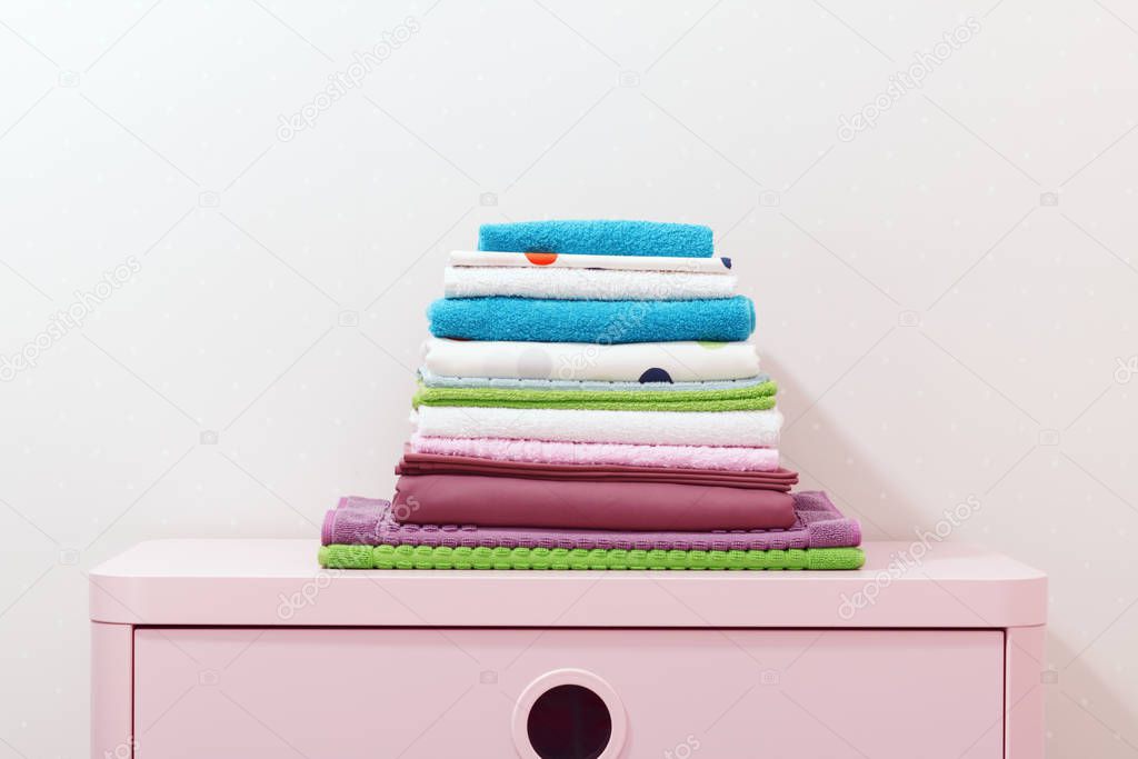 On the dresser there is a stack of clean ironed bed linen, folded colored towels