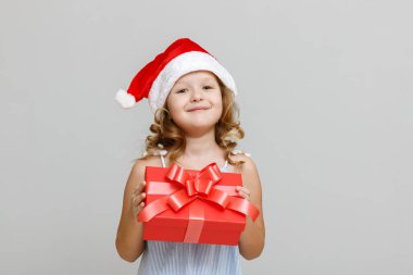 Gri arka planda mutlu, gülümseyen sarışın bir kızın portresi. Noel Baba şapkalı bir çocuk elinde hediyeli kırmızı bir kabuk tutuyor. Noel kutlaması kavramı