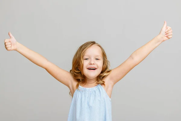 Gülümseyen küçük bir kız çocuğunun portresi gri bir arka planda ellerini kaldırdı. Başarı konsepti