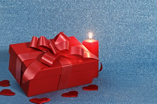 Closeup of a red box with a gift, a burning candle and hearts on a blue shiny background with a copy space. Valentine's day celebration concept — 스톡 사진