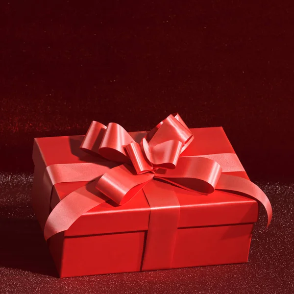 Κλείσιμο ενός κόκκινου κουτιού με δώρο σε κόκκινο γυαλιστερό φόντο με — Φωτογραφία Αρχείου