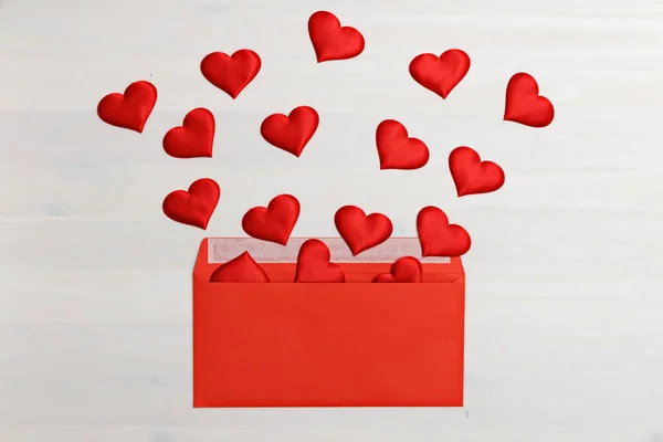 Червоні серця, що вилітають з червоної паперової оболонки на білому дерев "яному тлі. Святкування Дня Валентина — стокове фото