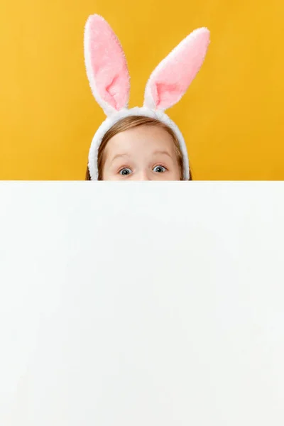 Frohe Ostern. Das lustige kleine Mädchen mit Hasenohren versteckt sich wegen eines leeren Banners. das Kind erbeutet Eier — Stockfoto