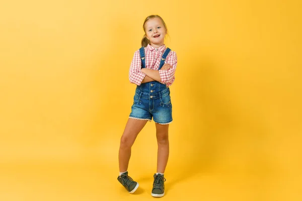 Fröhliches kleines blondes Mädchen steht vor der gelben Wand — Stockfoto