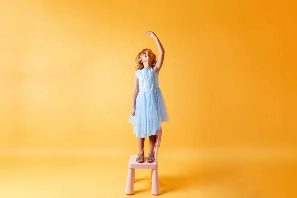 A little child girl in a blue dress is standing on a chair and m — 스톡 사진