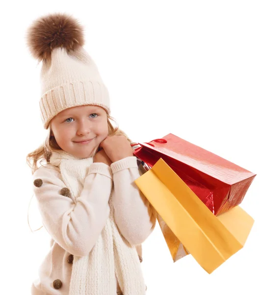 Una bambina in un cappello a maglia con pompon, sciarpa e maglione, tiene in mano sacchetti di carta multicolore. Isolato su sfondo bianco — Foto Stock