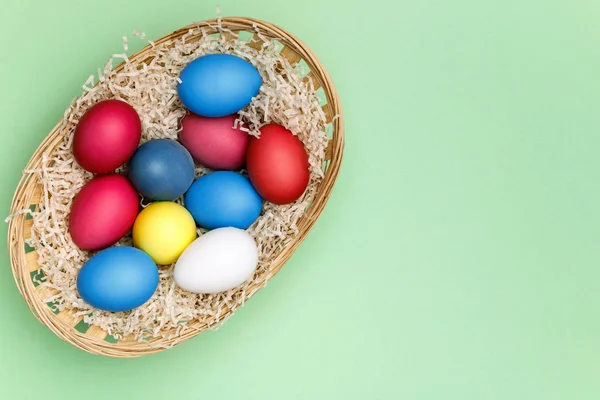 ミントの背景に色付きの卵を持つイースターバスケット。スペースのコピー — ストック写真