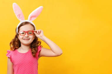 Happy easter. Beautiful little girl in rabbit ears and glasses on a yellow background. The child close up with copy space