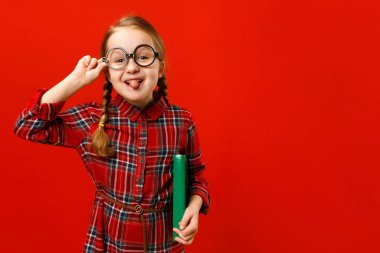 Gözlüklü, kırmızı arka planda kitabı olan neşeli bir çocuk. Küçük kız aylak aylak dolaşıyor ve dil gösteriyor..