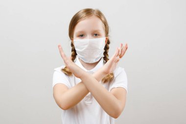 Korunaklı tıbbi maske takan küçük bir kız koronavirüs salgını sırasında elleriyle durdurma hareketi gösteriyor. Gri arkaplanda bir çocuğun portresi.