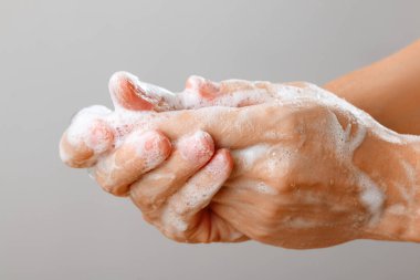 Gri arka planda sabunla ellerini yıkayan kadına yakın durun. Koronavirüs virüsünün dezenfeksiyonunun hijyenik önlenmesi.