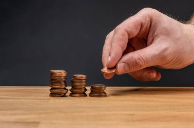 Koyu bir arka plana karşı tahta bir masaya madeni para istifleyen bir el..