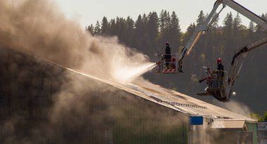 İki itfaiyeci bir depoda yangınla savaşıyor..