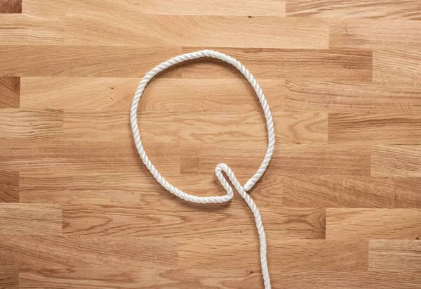 字母Q是用白色的绳子在一张木制桌子上形成的 — 图库照片