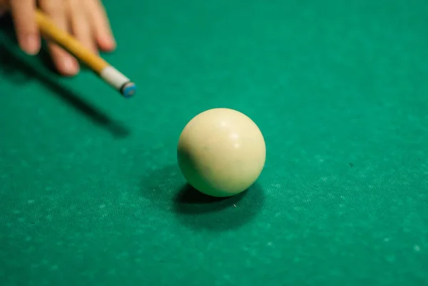 A hand holding a cue stick about to hit a white cue ball, playing pool.