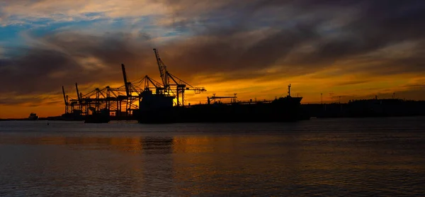 Silhouette eines Öltankers bei Sonnenuntergang. Containerhafen im Hintergrund.. — Stockfoto