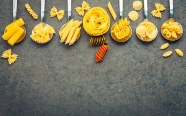 İtalyan gıda kavramı ve menü tasarımı. Makarna Farfalle, makarna A Riso, Orecchiette Pugliesi, Gnocco Sardo ve Farfalle çeşitli tür düz lay ile taş zemin üzerine metal kaşık kurulumunda.