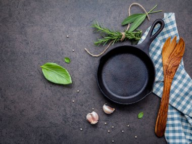 Karanlık taş zemin üzerinde boş eski dökme demir becerisi. Fotokopi alanı ile biftek konsepti yapmak için gerekli malzemeler. Çeşitli otlar ve baharat biberiyesi, adaçayı, defne yaprağı, fesleğen, sarımsak ve biber..