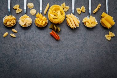 İtalyan gıda kavramı ve menü tasarımı. Makarna Farfalle, makarna A Riso, Orecchiette Pugliesi, Gnocco Sardo ve Farfalle çeşitli tür düz lay ile taş zemin üzerine metal kaşık kurulumunda.