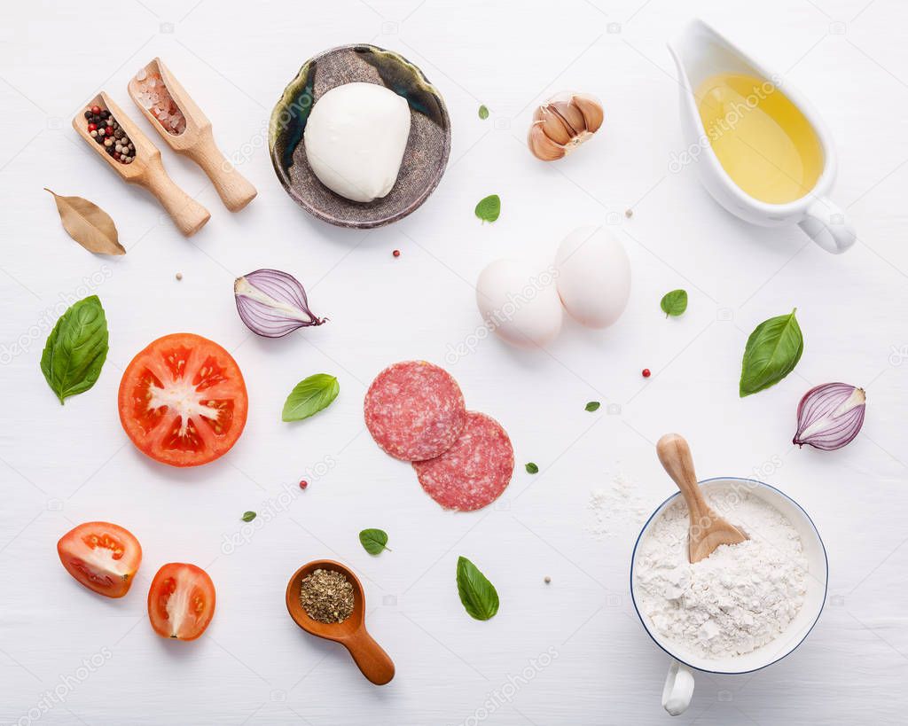The ingredients for homemade pizza with ingredients sweet basil ,tomato ,garlic ,bay leaves ,pepper ,onion and mozzarella cheese on white wooden background with flat lay.