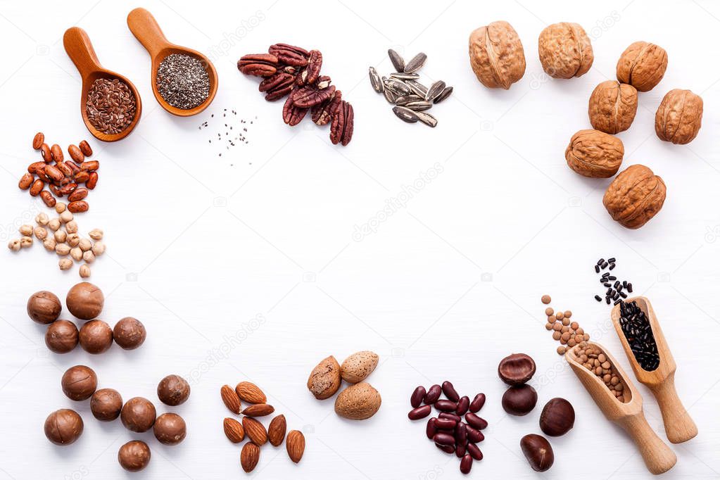 Spoon of various legumes and different kinds of nuts walnuts kernels ,hazelnuts, macadamia ,almond kernels,brown pinto ,red kidney beans and pecan set up on white wooden table.