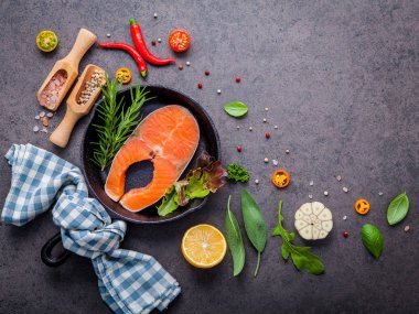 Eski dökme demir skille karanlık taş zemin üzerine somon fileto. Biftek kavramı kopya alanı ile yapmak için malzemeler. Çeşitli otlar ve baharatlarla biberiye, adaçayı yaprakları, fesleğen, sarımsak ve biber.