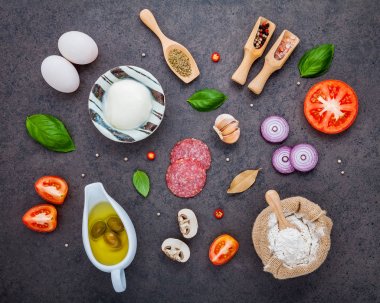 Malzemeler Reyhan, domates, sarımsak, defne yaprağı, biber, soğan ve mozzarella peyniri düz lay ile karanlık taş zemin üzerine ev yapımı pizza için malzemeler.