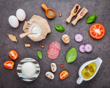 Malzemeler Reyhan, domates, sarımsak, defne yaprağı, biber, soğan ve mozzarella peyniri düz lay ile karanlık taş zemin üzerine ev yapımı pizza için malzemeler.