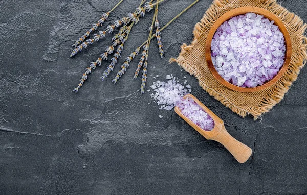 Aromatic purple bath salt with lavender flower on dark concrete background. Himalayan salt commonly used in cooking and for bath products such as bath salts.