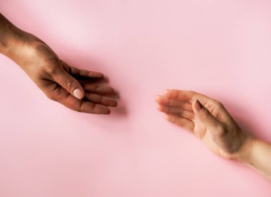 Siyah ve beyaz kadınlar pastel pembe arka planda el ele tutuşuyorlar. Minimum düz konsept. 