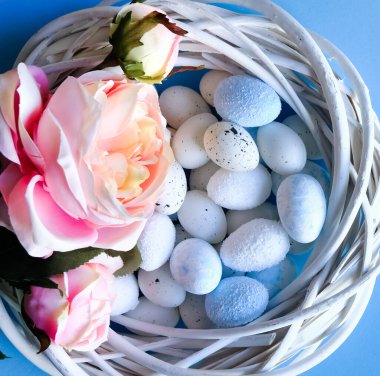 Yaratıcı Paskalya planı. Beyaz ahşap çelenk, pembe tekstil gülleri ve mavi pastel yumurtalar düz arka plan. Bahar tatili kavramı.