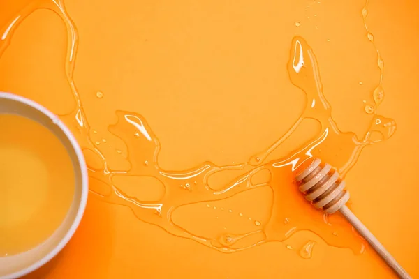 Agave syrup in bowl and wooden honey dipper on vivid orange background.