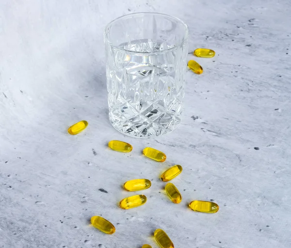 灰色の背景に水のガラスと医学黄色のカプセル — ストック写真