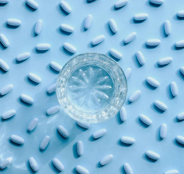 パステルカラーの背景に青い薬と水のガラス — ストック写真