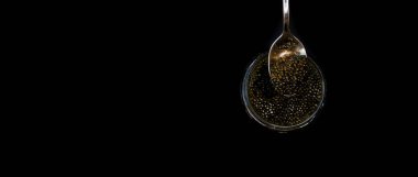 Cam kâse ve kaşık pankartıyla siyah havyar. Yüksek kaliteli gerçek mersin balığı siyah havyar, siyah arka planda lüks şarküteri.. 