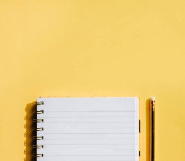 Pastel sarısı arka planda not defteri ve altın kalem. Okula geri dönüş konsepti. 