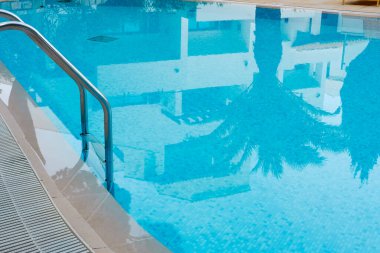 Palmiye ağacı ve tatil köyü mavi yüzme havuzu suyunda yansıyor.. 