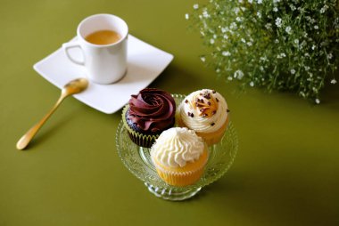 Krem peynirli vanilyalı kekler ve yeşil arka planda beyaz kahve. Tatlı yemek konsepti. 