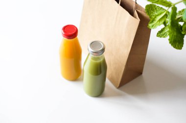 Yeşil ve turuncu detoks suyu, nane yaprakları ve beyaz arka planda kahverengi kağıt poşet bulunan cam şişeler. Sağlıklı yaşam tarzı kavramı. 