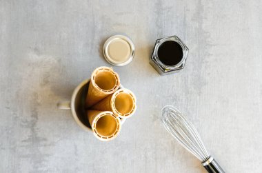 Cam kavanozlarda ev yapımı koyu çikolata sosu, dondurma külahları ve gri arka planda gümüş çırpı.. 