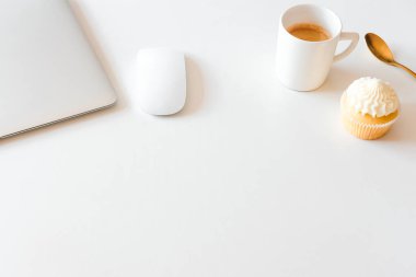 Bir fincan kahve ve kek, gümüş dizüstü bilgisayar beyaz masada. Ofis kavramında kahve molası. 