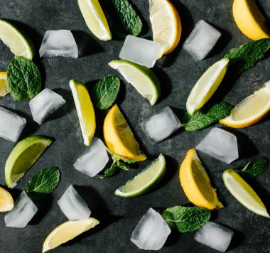 Taze kireç ve limon parçaları, nane yaprakları ve koyu arkaplanda buz küpleri. Yaz içeceği veya kokteyl konsepti.