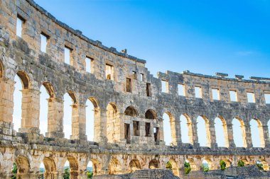 Hırvatistan 'ın Pula kentindeki antik miras. Antik Roma arenasının kemerleri. Tarihi amfi tiyatronun içi, mavi arka plandaki yüksek duvarların geniş açılı görüntüsü..