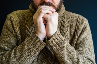 Mutsuz, üzgün, hırkalı, kafası çapraz kollarda dinlenen, yarı suratlı bir adam.