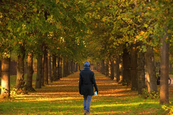 Genç adam elinde bir şişe suyla kulaklıkla ve paltoyla yürüyor.