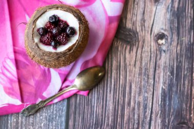 Ahşap bir arka plan üzerinde hindistan cevizi bir fincan yoğurt ile Berry tatlı. Böğürtlen, ahududu, yaban mersini, siyah kuş üzümü. Pembe peçete