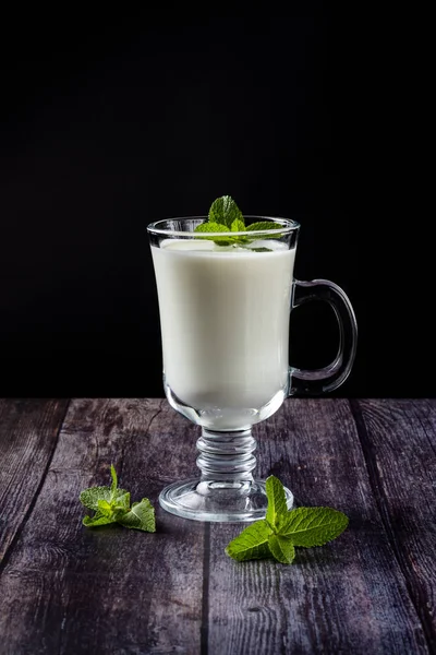 Ayran w szklance, kwaśny napój mleczny, jogurt, ozdobiony liściem mięty. Na drewnianym tle — Zdjęcie stockowe