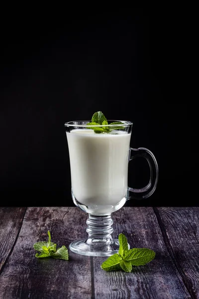 Ayran w szklance, kwaśny napój mleczny, jogurt, ozdobiony liściem mięty. Na drewnianym tle — Zdjęcie stockowe